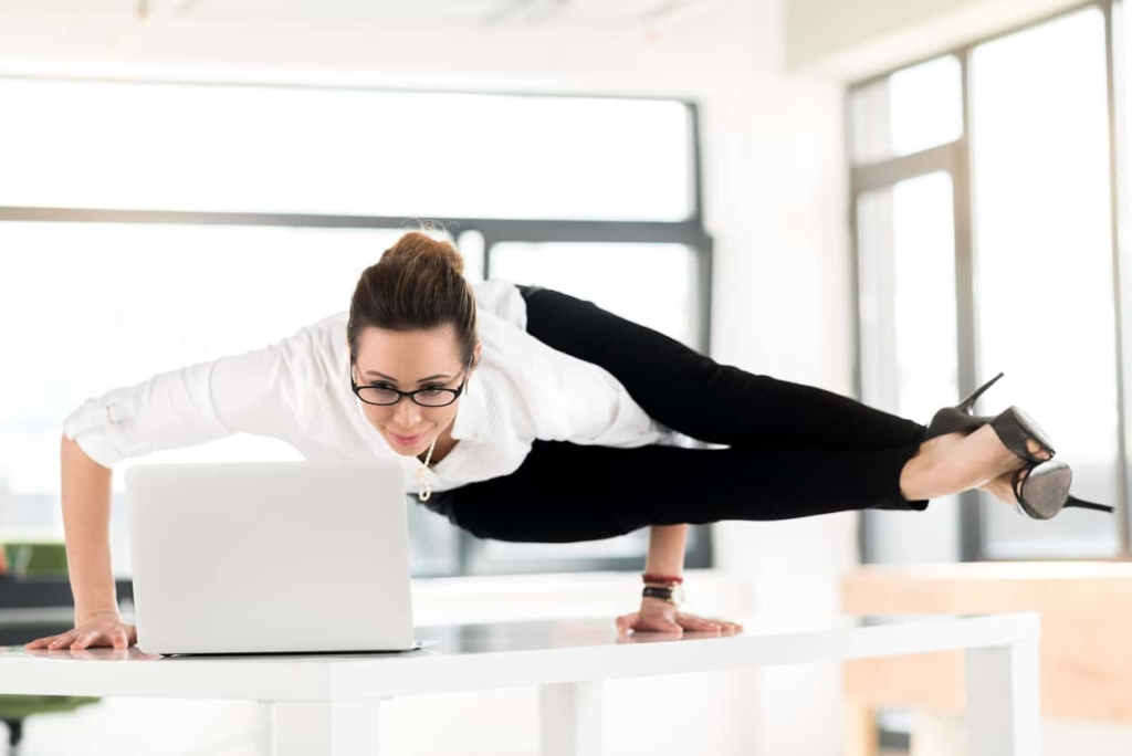 I need relaxation during my job. Female expressing happiness while looking at screen of notebook computer. She locating on desk in athletic position. Rest concept