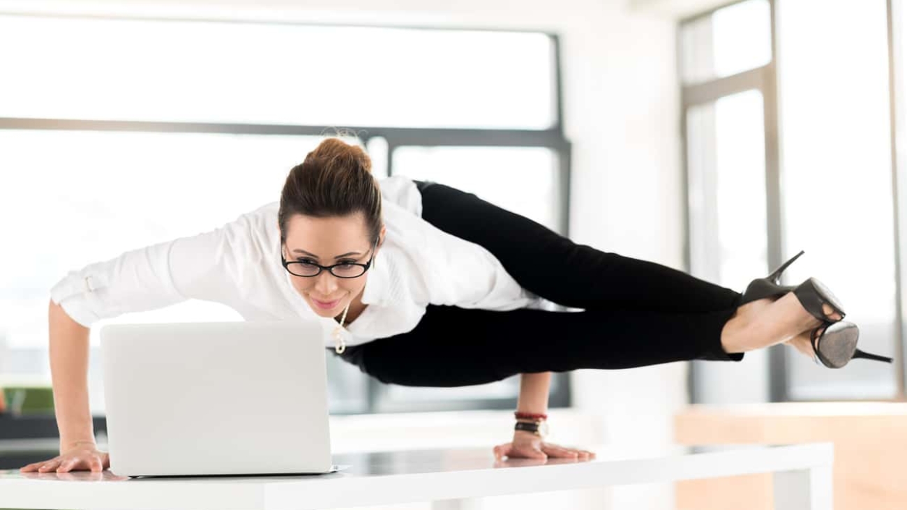 I need relaxation during my job. Female expressing happiness while looking at screen of notebook computer. She locating on desk in athletic position. Rest concept