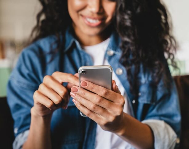 Cropped shot of an african-american young woman using smart phone at home.Smiling african american woman using smartphone at home, messaging or browsing social networks while relaxing on couch